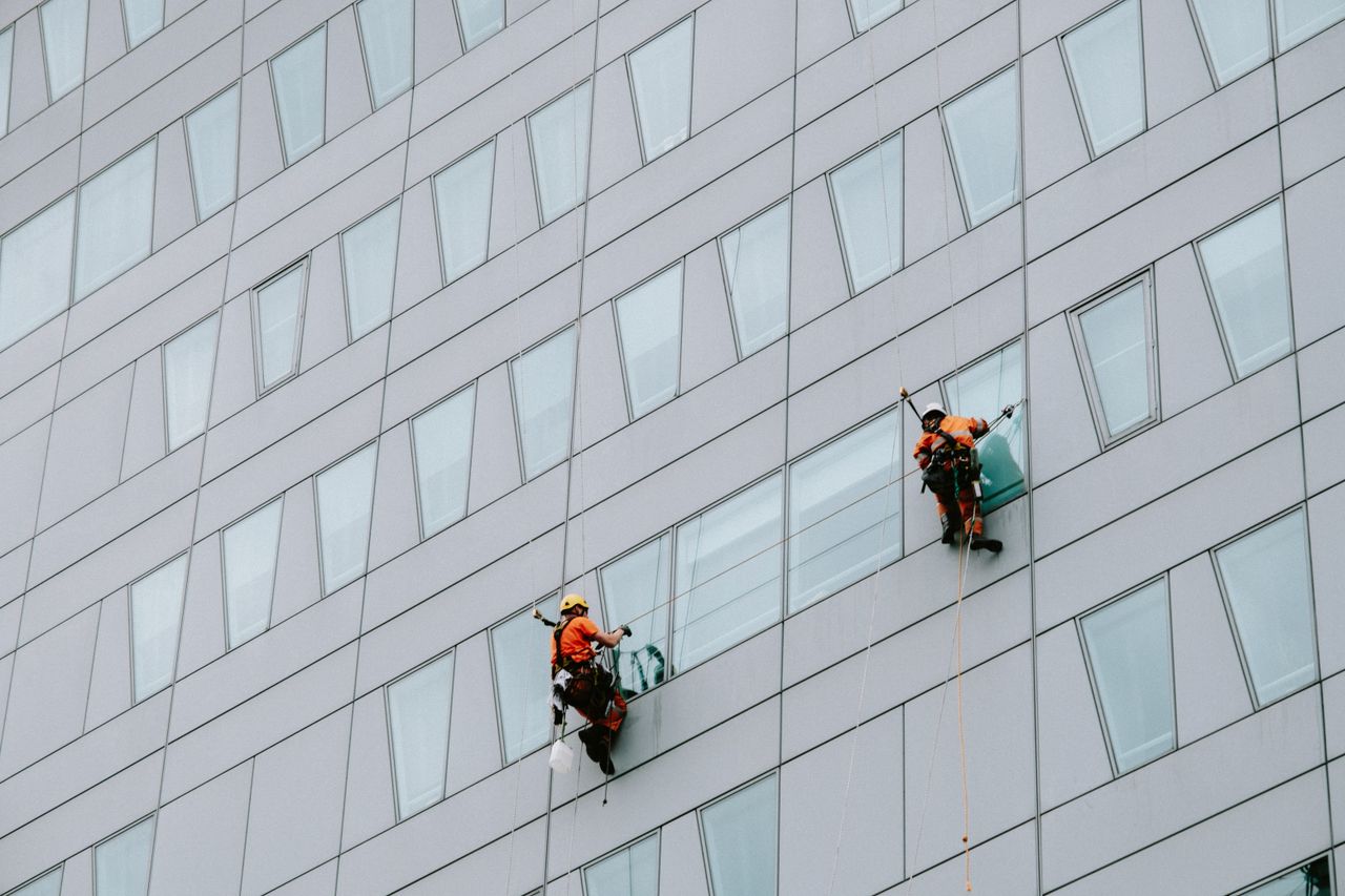 Window cleaners wearing safety equipment are washing the outside of a skyscraper.